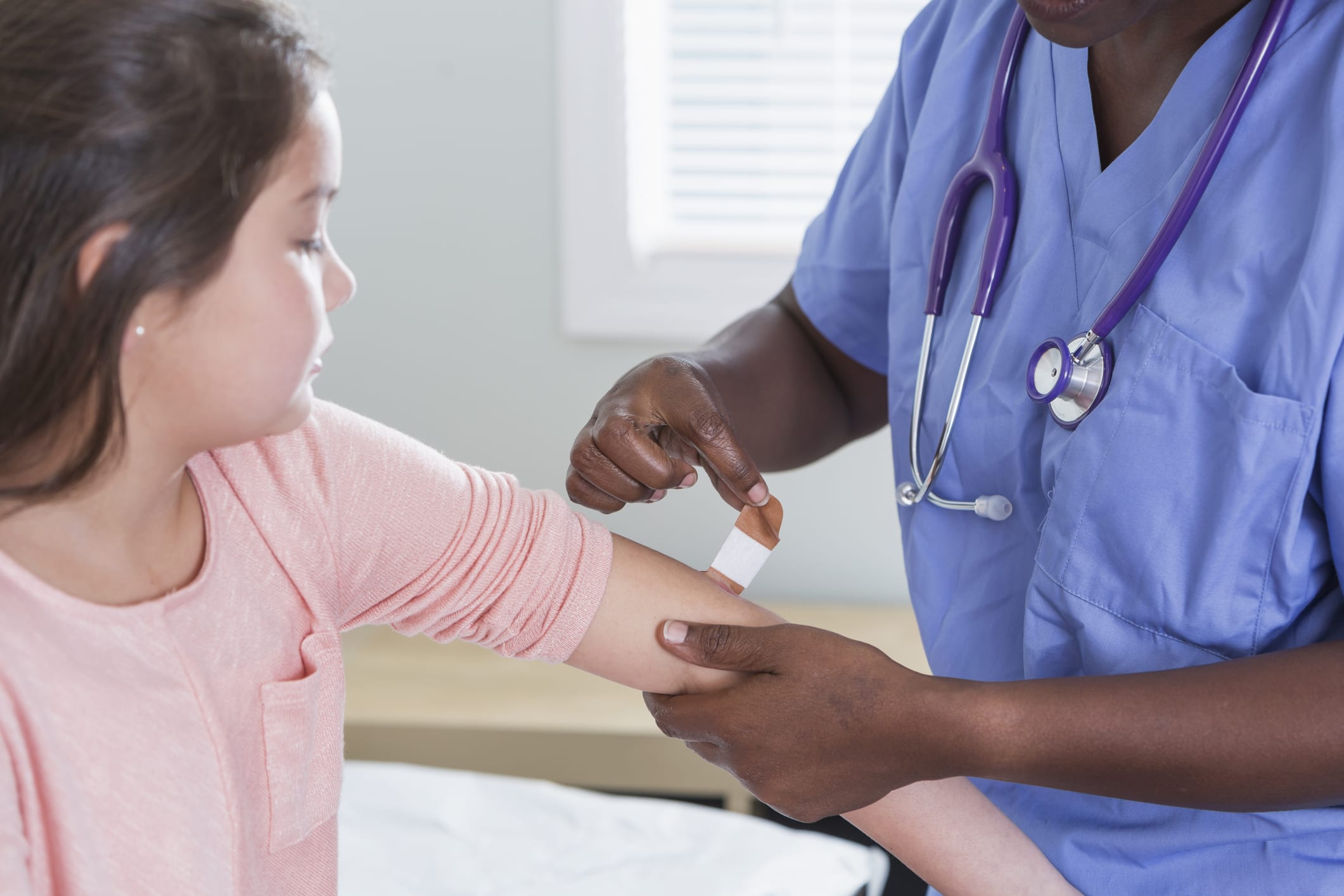 Black nurse putting adhesive bandage on girl's arm Cropped view of a female doctor or nurse smiling at the camera as she puts an adhesive bandage on the arm of her young patient, a 9 year old girl.